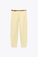 Pantalón chino color amarillo claro, de tiro medio, con bolsillos frontales y traseros. Incluye cinturón trenzado marrón.