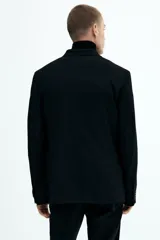 Blazer negro de corte slim fit, con solapas de muesca finas y ojal decorativo. Modelo de botonadura sencilla con bolsillo superior insertado, bolsillos delanteros con solapa, dos bolsillos en el interior y botones decorativos en los puños. Abertura doble atrás.