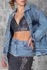 Campera de jean celeste con apliques de strass y cadenas en hombros y bolsillos.