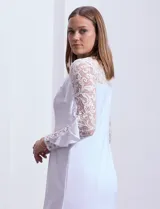 Vestido blanco de seda fría, corte midi ajustado al cuerpo, con mangas largas de encaje con brillos y aplique fruncido en el hombro.