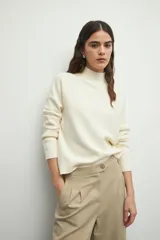 Polera color crema de tejido de punto, con cuello alto y mangas largas abullonadas con detalle de bordado trenzado.