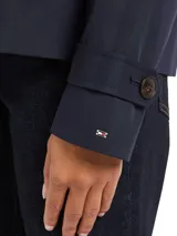 Gabardina corta azul marino de Tommy Hilfiger, con botonadura simple, cuello inglés, trabillas en los hombros, solapa de protección delantera y trasera, puños con tira y botón, y logo metálico en el puño.