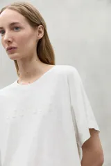 Camiseta blanca de algodón orgánico con cuello redondo y mangas cortas. Estampado frontal con la palabra "Because" en relieve.