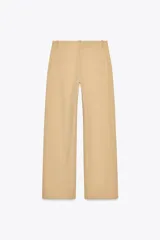 Pantalón color beige de tiro alto con bolsillos delanteros y falsos bolsillos de vivo en la espalda, de pierna ancha y corte recto. Cierre frontal con cremallera y botón.