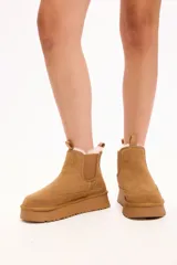 Bota tipo chelsea color camel, confeccionada en gamuza con interior forrado en piel sintética. Presenta elásticos laterales, tirador en la parte trasera y plataforma alta con suela dentada.