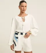 Blusa blanca de poliéster satinado, con mangas largas abullonadas, cuello con abertura en forma de gota y lazo con colgantes de corazón.