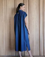 Túnica celeste de corte recto, con cuello camisero, mangas cortas, tajos laterales y cierre frontal con botones.