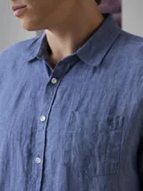 Camisa azul de lino con botones blancos, manga larga y bolsillo en el pecho.