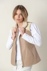 Chaleco color beige con cuello alto y cierre frontal con cremallera. Presenta detalles de piel sintética color crema en los hombros.
