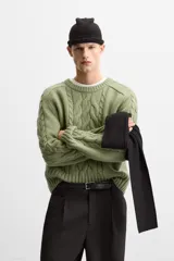 Sweater verde claro de punto con cuello redondo y mangas largas. Presenta diseño de trenzas en el centro y en las mangas.