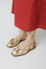 Sandalias bajas de cuero color marrón con tiras finas que se atan al tobillo.