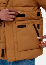 Campera acolchada marrón de Carhartt WIP, modelo Munro Jacket. Confeccionada en popelina de nailon repelente al agua y forro de tafetán de nailon. Relleno de plumón artificial, puños y bajo ajustables, cierre frontal con cremallera bidireccional oculta, múltiples bolsillos delanteros con cremallera y etiqueta de tela con logo en el frente.