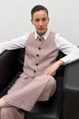 Chaleco de vestir sin mangas, color beige con estampado de cuadros pequeños en tonos rojizos y marrones. Tiene cuello solapa y cierre frontal con botones oscuros.