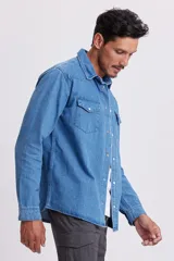 Camisa de jean celeste de manga larga con cuello clásico, cierre con botones a presión y dos bolsillos con solapa abotonada en el pecho.