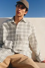 Camisa blanca con diseño a cuadros grises, de corte holgado, manga larga y cuello inglés.