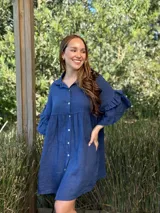 Vestido camisero azul de lino italiano, con cuello camisero, botones frontales, mangas 3/4 con doble volado y bolsillos laterales.