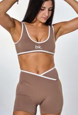 Conjunto deportivo color marrón con detalles en blanco, compuesto por un top con logo "bk." y unos shorts de tiro alto.