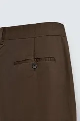 Pantalón relaxed fit color marrón confeccionado en tejido de algodón con estructura twill. Cintura con pliegues frontales, bolsillos laterales en cadera y detalle de bolsillos traseros de doble vivo con botón. Cierre frontal con cremallera y botón.