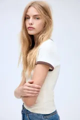 Remera blanca entallada de punto suave con cuello y mangas con ribete marrón.