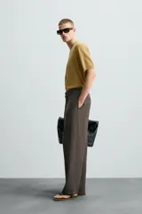 Pantalón marrón de corte ancho, con cintura ajustable con cordón, bolsillos delanteros y traseros tipo parche, detalle de costuras verticales en el frente y cierre frontal con cremallera y gancho metálico oculto.