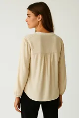 Blusa celeste de viscosa con cuello en V y mangas largas. Presenta detalles de broderie en los hombros y corte holgado.