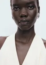 Mono largo color crudo, con escote halter, sin mangas, con cierre de botones frontal y cinturón tipo lazo en la cintura.