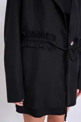 Blazer marrón con solapas de muesca, cierre frontal con lazo y mangas largas. Presenta volados a lo largo de las costuras laterales del pantalón a juego.