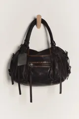 Bolso de mano pequeño de cuero negro con efecto lavado y envejecido intencional, presentando variaciones naturales en textura y color. Tiene asas de mano trenzadas y múltiples cierres externos con tiradores de cuero.