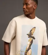 Remera overboxy color crema con estampa frontal de una mujer con un pájaro en la cabeza y lettering bordado.