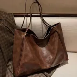 Bolso tipo tote bag color beige claro, de material sintético liso con caída suave. Posee dos asas delgadas para llevar al hombro.