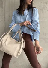 Camisa celeste de manga larga con cuello mao y cierre frontal con botones. Presenta detalles de broderie en el frente y mangas.