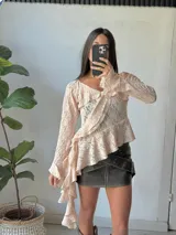 Blusa de encaje color rosa pálido con volados asimétricos y mangas largas acampanadas.