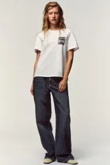 Camiseta blanca de algodón con cuello redondo y mangas cortas. Estampado frontal con texto "Meet me at Palais Lomtam, 7, Passage des Rêveries" enmarcado en un diseño ondulado.