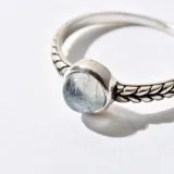 Anillo plateado con dije circular de piedra blanca.