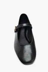Zapato plano tipo bailarina en piel color negro, con tira sobre el empeine y hebilla metálica ajustable.