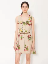 Vestido corto color beige con estampado floral, cuello en V, bolsillos frontales con solapa y botones dorados, y cinturón marrón de cuero vacuno con hebilla dorada.