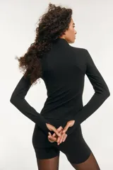 Campera deportiva negra de corte ajustado con cuello elevado, cierre frontal con protección para el mentón y bolsillos laterales con cierre. Mangas largas con abertura para el pulgar.