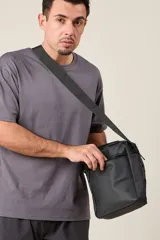 Bandolera negra con correa ajustable, cierre superior y bolsillo frontal con cierre.