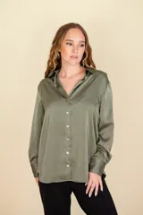 Camisa verde oliva de satén 100% poliéster, con cuello clásico, cierre frontal abotonado con botones de nácar, corte más largo en la espalda y doble botón en los puños.