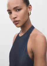 Mono largo de denim azul oscuro, sin mangas, con cuello halter y escote en la espalda. Presenta un corte recto y holgado en las piernas.