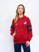 Campera de felpa roja con capucha, cierre frontal y bolsillos laterales. Presenta cortes y cambios de color en azul y blanco en mangas y laterales. Incluye logo de Umbro bordado en el pecho y escudo del Club Nacional de Football en el lateral superior derecho.