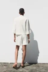 Blazer blanca de cuello solapa y manga corta con vuelta. Bolsillos delanteros de vivo y cierre frontal cruzado con botones.