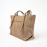 Bolso tote color marrón claro con textura tipo arpillera, doble asa fina color camel y detalle de borla decorativa.