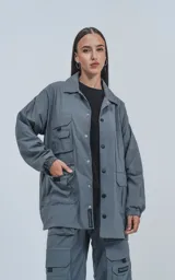 Campera gris con broches en el delantero, forrada con red, múltiples bolsillos con detalles en réflex y puños elásticos en las mangas. Confeccionada en poliéster y calce oversize.