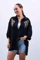 Camisa negra de mangas largas con puños abotonados y bordados dorados en el frente.