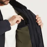 Campera negra con cuello de piel sintética, cierre con botones tipo tanca, bolsillos frontales con solapa y bolsillo vertical en el pecho. Corte recto y largo a la cadera.