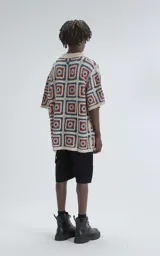 Camisa de manga corta tejida a crochet en punto abierto, con cuello tipo polo y cierre frontal con botones. Diseño con cuadrados de colores beige, naranja y azul. Corte oversize.