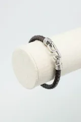 Pulsera de cuero trenzado color marrón con cierre metálico plateado con forma de letra "H".