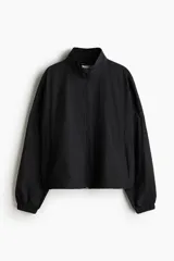 Campera negra de nylon repelente al agua y rompevientos con cuello elevado, cierre con protección para el mentón y bolsillos laterales con cierre. Modelo con hombros caídos, orificios de ventilación en las sisas y mangas murciélago con puños elásticos. Panel de ventilación en malla en la parte baja de la espalda y cordón para ajustar elástico con topes en el bajo. Forro de malla.