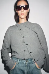 Chaqueta de punto color rosa pálido, con cuello redondo y cierre frontal de botones oscuros. Presenta mangas largas y un corte a la cintura.